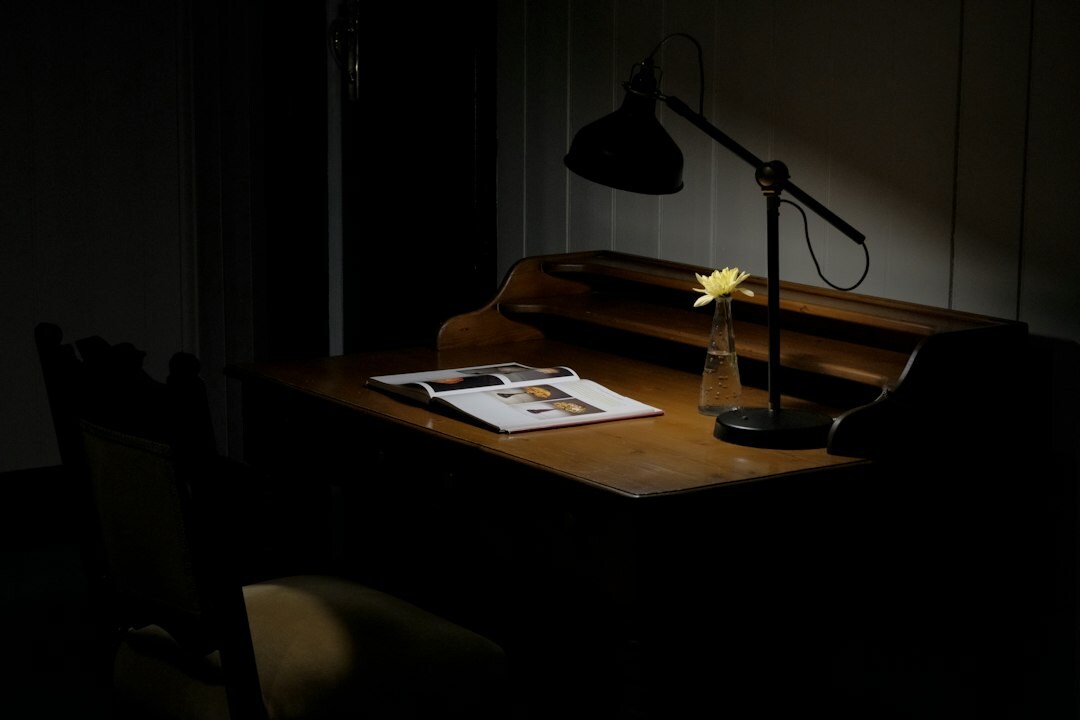 Old wooden writing desk with typewriter, notebook and dim lamp at night